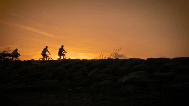 Silhouettes of people riding bikes and walking on a boardwalk at sunset