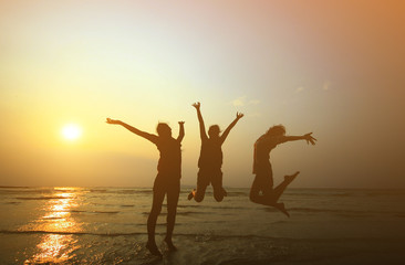 Fototapeta premium Silhouette of three young girls jumping with hands up on the be