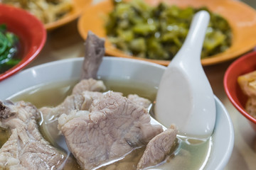 Bak kut teh served on table with vegetables, tofu and chili side dishes, selective focus on front object