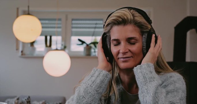Attractive woman enjoying her music indoors at home as she listens to the soundtracks on stereo headphones with her eyes closed and a smile of pleasure