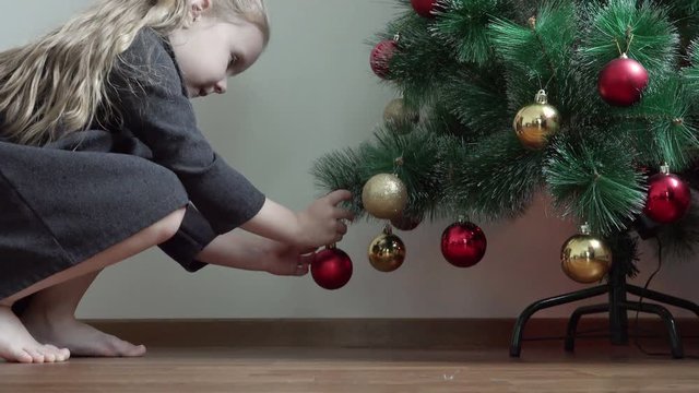 a little girl with bare feet coming to the Christmas tree and hang a garland on a branch in the form of New Year's decorations