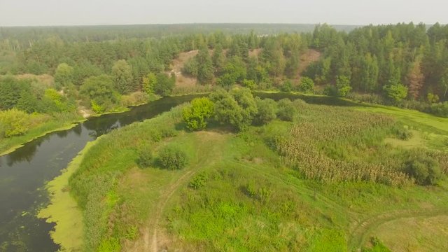 Beautiful summer aerial shot of river, grass field and forest on the hill in countryside at the middle of the day