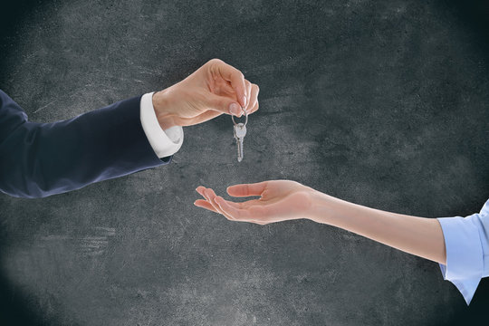 Male hand giving a car key to woman's hand on grey background