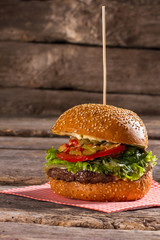 Tasty hamburger on wooden stick. Old table with big burger. Special sauce and juicy meat. Food that's bad for health.