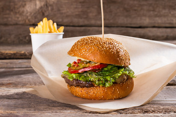 Burger on wax paper. Beef burger on old table. Food served in retro diner. Delicious well-made meal.
