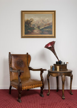 Retro leather armchair, a 1911 old phonograph with three cylinder records on round coffee table and hanged painting on red carpet
