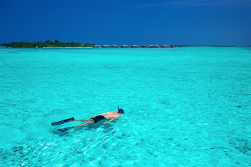 Young man snorkeling in tropical lagoon with over water bungalows