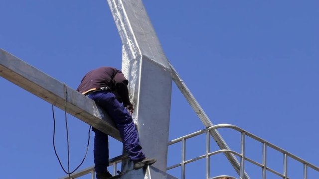 Man welding a metal construction sitting on the beam dangerously high