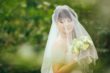 Elegant brunette bride posing outdoors with a bouquet on her wedding day