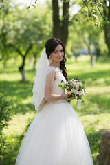 Elegant brunette bride posing outdoors with a bouquet on her wedding day