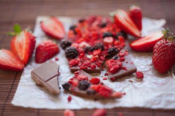 Handmade chocolate with fresh and dried berries, raspberries, strawberries, black currants, blackberries, cocoa powder, on wooden background in rustic style