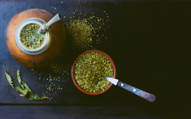 Yerba mate in calabash and dry herb in clay bowl on black background. Top view