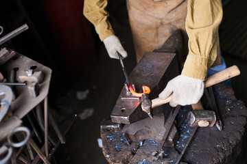 Male hands in the production process of metal products handmade on the anvil