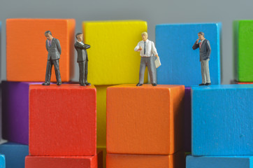 Miniature people on stack of colorful wooden cube building blocks