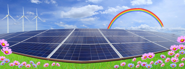 Solar panels with wind turbines on blue sky and rainbow with fie