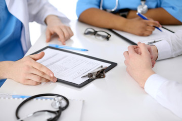 Two doctors and male patient discussing medical history at the table, close up