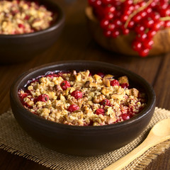Redcurrant crumble or crisp with oatmeal and walnut on top baked in rustic bowl, photographed on dark wood with natural light (Selective Focus, Focus in the middle of the crumble)