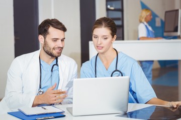 Doctor colleagues using laptop while discussing 