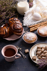 Chocolate Danish rolls, cupcakes eggs and cup of cocoa. Breakfast served on wooden table, decorated with heather.