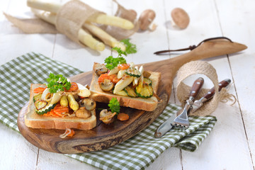 Vegetarischer Toast mit gebratenem weißen Spargel und gemischtem Gemüse, auf einem Holzbrett serviert - Vegetarian toast with fried white asparagus and mixed vegetables, served on a wooden board