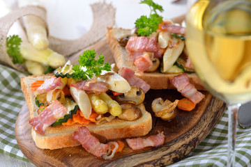 Deftiger Toast mit gebratenem Gemüse und Speck, mit Weißwein serviert - Hearty toast with fried vegetables and bacon, served with white wine