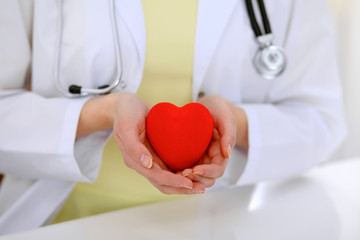 Female doctor with stethoscope holding heart.  Patients couple sitting in the background