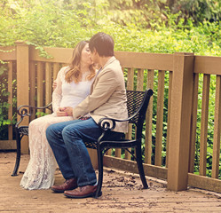 Expecting mom and dad kissing on patio bench outdoors