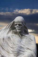 Statue of the Death with a veil with a sunset landscape at the background