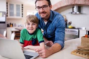 Portrait of father and son using laptop in kitchen