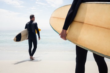 Rear view of man walking with surfboard on the beach - obrazy, fototapety, plakaty
