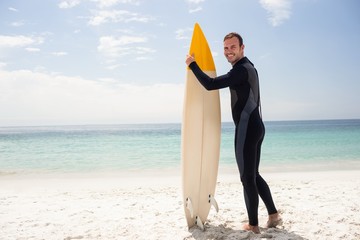 Happy surfer holding a surfboard on the beach - obrazy, fototapety, plakaty