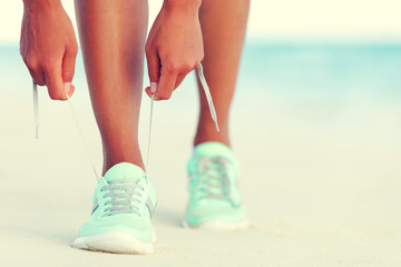 Healthy runner woman tying running shoes laces getting ready for beach jogging. Closeup of hands lacing cross training sneakers trainers for cardio workout. Female athlete living a fit and active life - obrazy, fototapety, plakaty