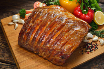 Grilled pork ribs and various vegetables on a chopping wood