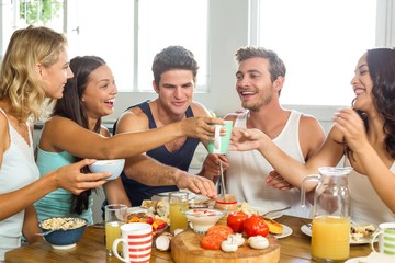 Cheerful young friends having breakfast at table in house