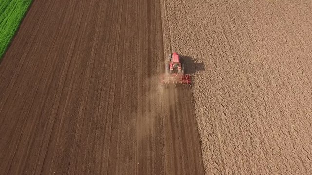Tractor cultivating arable land for seeding crops, aerial view