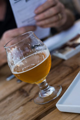 Glass of beer on a restaurant table, with a customer holding a menu behind it.