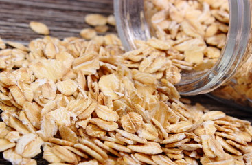 Oat flakes spilling out of jar on wooden background