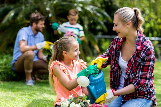 Happy Mother And Daughter Watering Flowers In Yard 