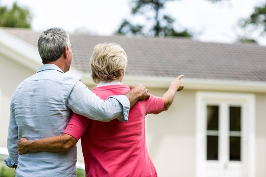 Senior couple looking at house while standing in yard 