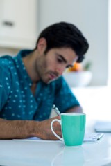 Man writing on clipboard with coffee mug on table