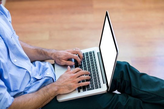 Mid-section of man sitting on floor and using laptop
