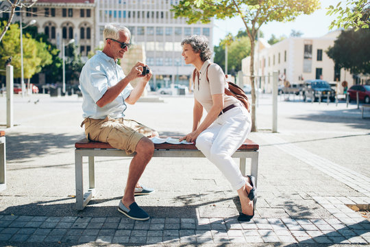 Senior tourist sitting on a bench looking pictures on camera