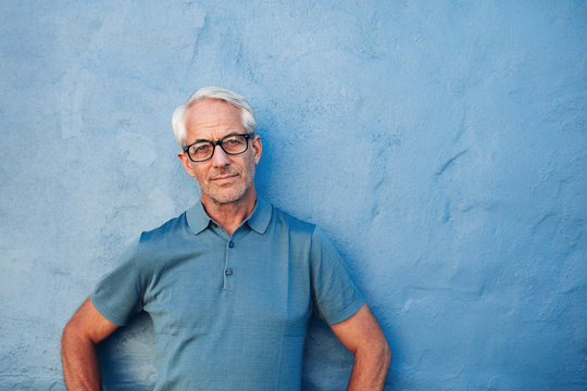 Mature Man Standing Against A Blue Wall