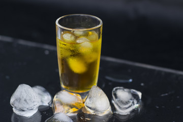 A glass of cognac with ice on black background, close-up
