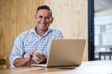 Smiling senior man using smartphone and laptop