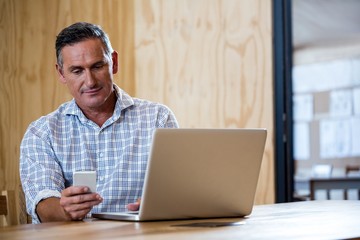 Man text messaging on phone while using a laptop