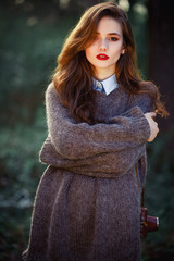 young beautiful girl with long hair brown hair, expressive cheekbones free warm sweater and pants with a film camera in hand walks on spring park