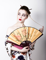 beautiful girl dressed as a geisha, she holds a chinese fan. Geisha makeup and hair dressed in a kimono. The concept of traditional Japanese values