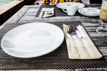 Dinner place setting. A white plate with fork and spoon. Table setting in restaurant interior