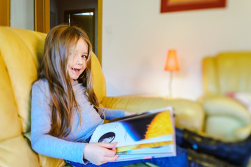 Cute little girl with long hair reading children book in livivng
